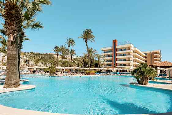 Bilde av et bassengområde med solsenger, parasoller og palmer foran et hotell. (AI-generert tekst)