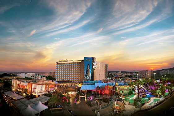 En utsikt over et feriehotell med en fargerik temapark foran en solnedgang. (AI-generert tekst)