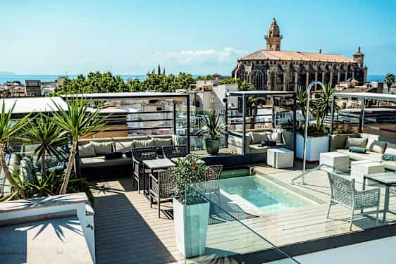 Takterrasse med sittegrupper, planter og et lite basseng, med utsikt mot en kirke. (AI-generert tekst)