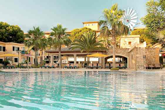 Et svømmebasseng foran en bygning med palmer og en liten vindmølle synlig. (AI-generert tekst)