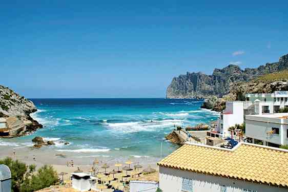 En vakker kyst med turkist hav, sandstrand og parasoller. Det finnes klipper og bygninger med lyse tak. (AI-generert tekst)