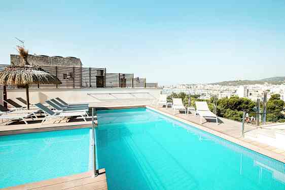 Et svømmebasseng på en terrasse med solsenger og utsikt over en by. (AI-generert tekst)