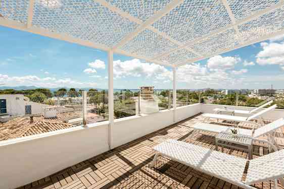 En takterrasse med solsenger og et bord. Terrassen har en perforert takdekke og glassrekkverk med utsikt over byen og havet. (AI-generert tekst)