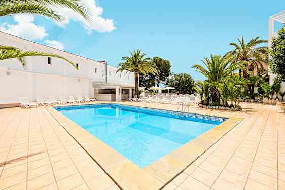 Bilde som viser et basseng med lyseblått vann, omgitt av en solterrasse med solsenger og palmer. (AI-generert tekst)