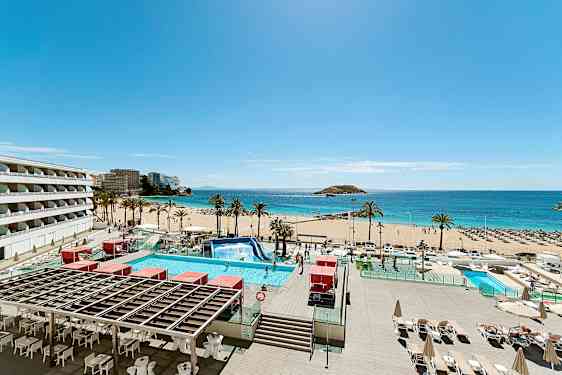 Bilde av en solrik strand med palmer, turkist vann og et basseng i forgrunnen. Bygninger vises til venstre. (AI-generert tekst)