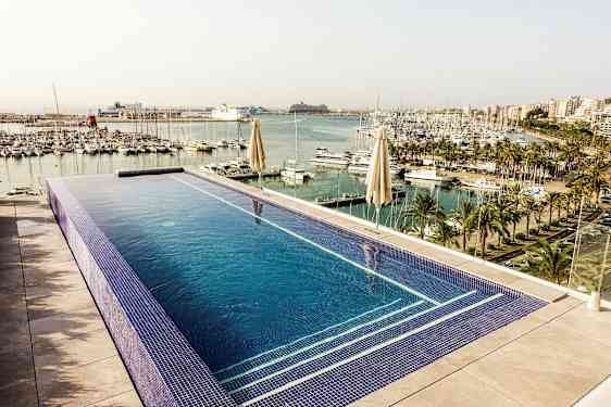 Bilde av et evighetsbasseng med utsikt over en småbåthavn med palmer og fleretasje bygninger i bakgrunnen. (AI-generert tekst)