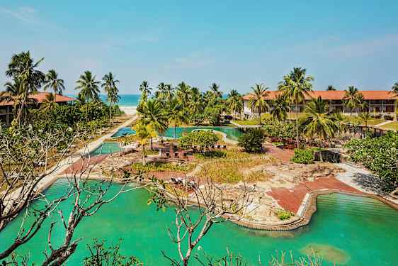 Hotellkompleks med bassenger, palmer og en sandstrand i bakgrunnen. (AI-generert tekst)