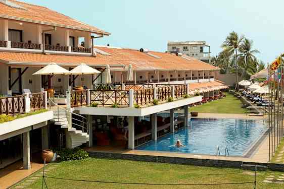 Hotell med utendørsbasseng, terrasser og solsenger. En person svømmer i bassenget. (AI-generert tekst)