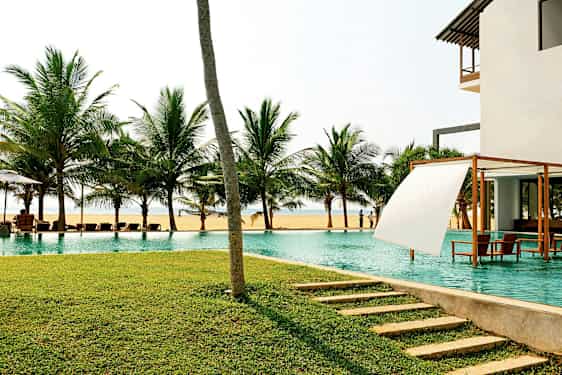 Et basseng ved havet med palmer i bakgrunnen og en plen i forgrunnen. (AI-generert tekst)