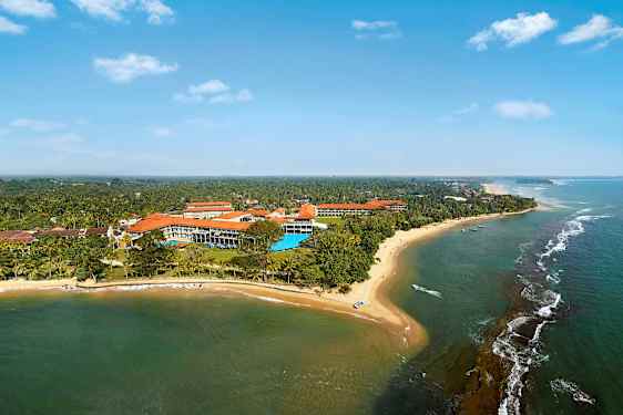 Et flyfoto av en kystlinje med sandstrand, hav og bygninger omgitt av vegetasjon. (AI-generert tekst)