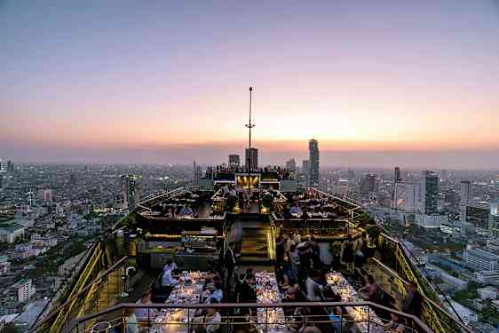 Takbar ved solnedgang med restaurantgjester og panoramautsikt over byens skyline. (AI-generert tekst)