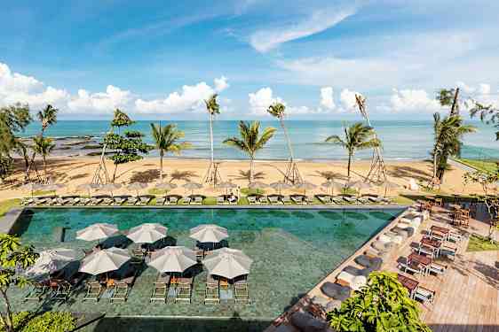 En strand med palmer i bakgrunnen og et basseng med solsenger og parasoller i forgrunnen. (AI-generert tekst)