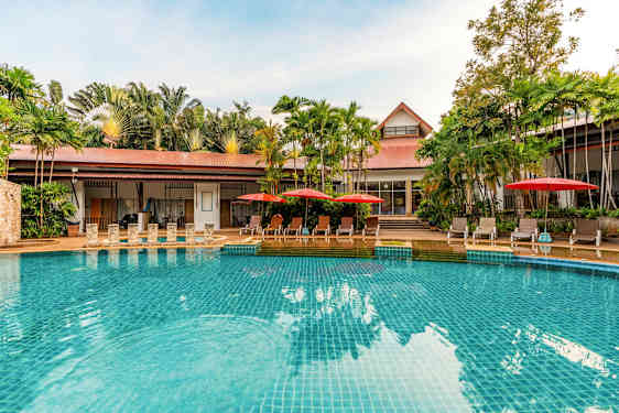 Et basseng med klart blått vann, omgitt av solsenger med røde parasoller og grønne palmer i bakgrunnen. (AI-generert tekst)