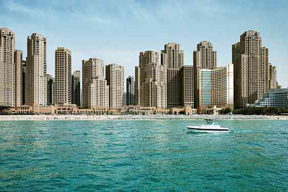 En strandlinje med høye bygninger i bakgrunnen og en båt på sjøen. (AI-generert tekst)