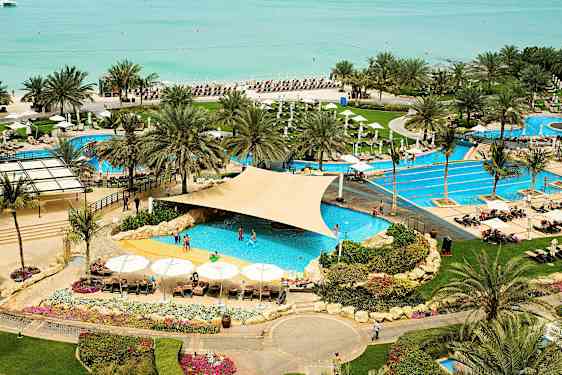 Et feriested med bassengområde nær stranden, omgitt av palmer og solsenger. (AI-generert tekst)