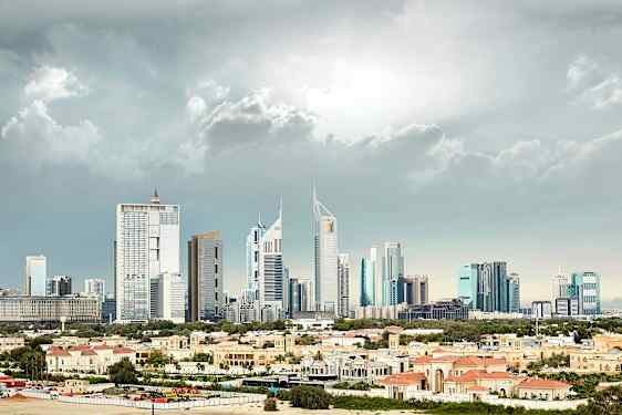 Bilde av en by med høye, moderne bygninger i bakgrunnen og lave bygninger med rødlige tak i forgrunnen. (AI-generert tekst)