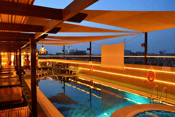 Et basseng på en terrasse med solsenger og bord, med belysning om kvelden. (AI-generert tekst)