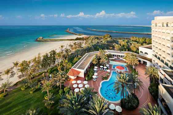 Et bilde av et hotell ved stranden med et utendørs basseng, solsenger og omkringliggende grøntområder. (AI-generert tekst)