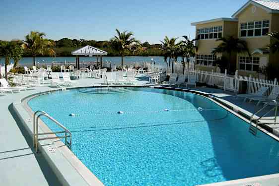 Bilde av et utendørs basseng omgitt av solsenger og parasoller. I bakgrunnen sees en liten innsjø omgitt av grøntområder. (AI-generert tekst)