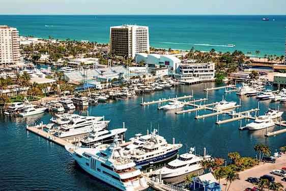 En småbåthavn med luksusyachter og båter ved siden av urbane bygninger og grøntområder, med havet i bakgrunnen. (AI-generert tekst)