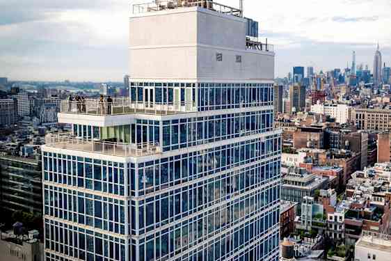 Høy bygning med glassfasade og terrasse, omgitt av bymiljø. (AI-generert tekst)