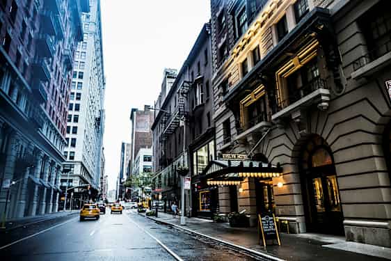 En bygate med høye bygninger lags sidene og taxibiler som kjører på veien. Evelyn Hotel-skiltet er synlig til høyre. (AI-generert tekst)