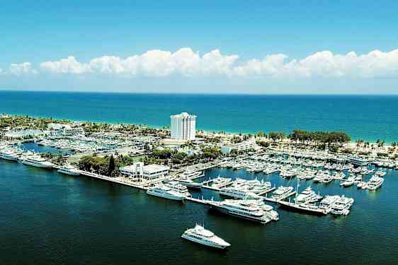 En marina med båter og yachter ved kysten med en bygning og et hotell i bakgrunnen. (AI-generert tekst)