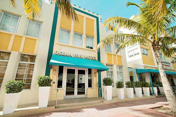 En hotellfasade med turkis baldakin og gule detaljer, omgitt av palmer. (AI-generert tekst)