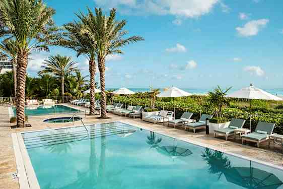 Bilde av et hotellbassengområde med palmer, solsenger og parasoller ved kanten. Havet kan ses i bakgrunnen. (AI-generert tekst)