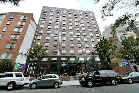 Et boligbygg med glassinngang og parkerte biler foran. (AI-generert tekst)