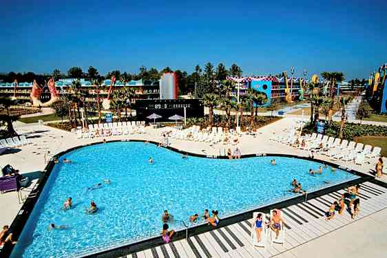 Et svømmebasseng omgitt av solstoler på et feriested. Bakgrunnen viser bygninger og dekorasjoner. (AI-generert tekst)