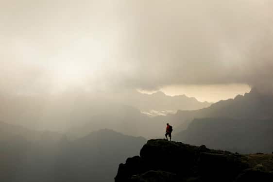 En turgåer står på en fjelltopp med tåkete daler og fjell i bakgrunnen. (AI-generert tekst)
