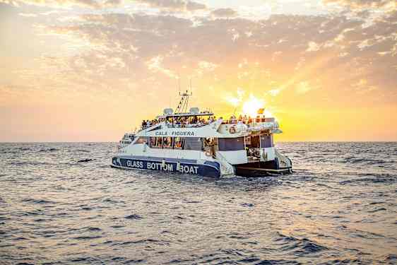 En glassbunnbåt med mennesker om bord seiler på havet under en solnedgang. (AI-generert tekst)