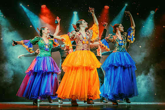 Tre personer kledd i fargerike tradisjonelle drakter danser på en opplyst scene. (AI-generert tekst)