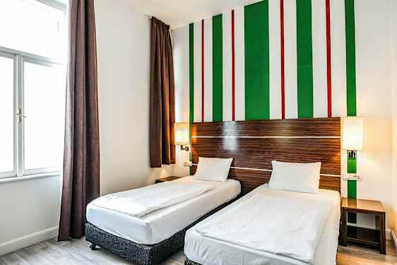 Et hotellrom med to enkeltsenger, brune gardiner og en veggdesign med grønne, hvite og røde striper. (AI-generert tekst)