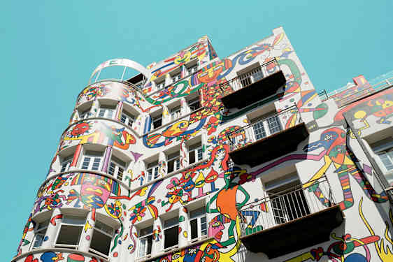 Bygning med fargerike abstrakte malerier på fasaden mot en klar blå himmel. (AI-generert tekst)