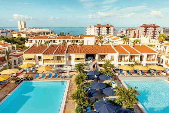 Leilighetsbygninger med røde tak, bassengområder og hav i bakgrunnen. (AI-generert tekst)