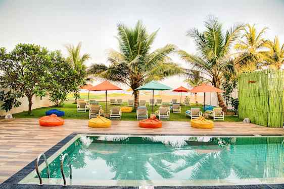 Et basseng med solsenger og fargerike parasoller i en hage omgitt av palmer. (AI-generert tekst)