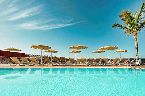 Et basseng med solsenger og parasoller under en klar blå himmel. (AI-generert tekst)