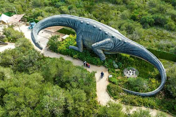 En stor dinosaurstatue omgitt av grønt sett ovenfra. (AI-generert tekst)