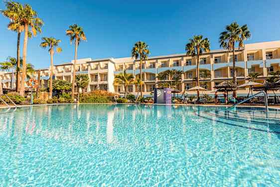 Et utendørsbasseng omgitt av palmer og et hotell i bakgrunnen. (AI-generert tekst)