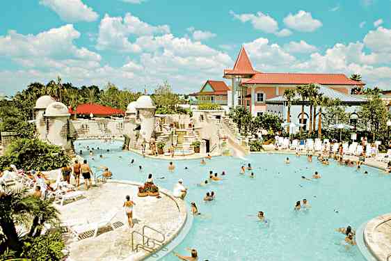 Et utendørsbasseng omgitt av mennesker, solsenger og bygninger. (AI-generert tekst)