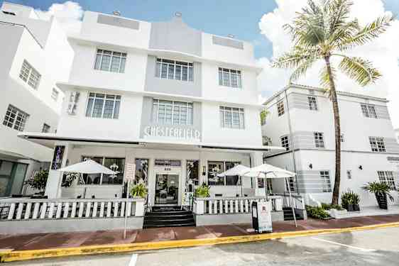 Et hvitt hotell i moderne arkitektur med store vinduer og en veranda med parasoller. (AI-generert tekst)