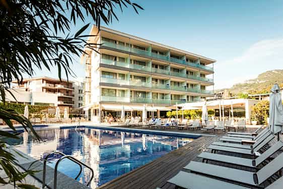 Bilde av et hotell med svømmebasseng og solsenger utendørs. (AI-generert tekst)