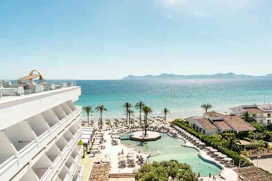 En utsikt over hotellbasseng, strand og hav med palmer og bygninger. (AI-generert tekst)