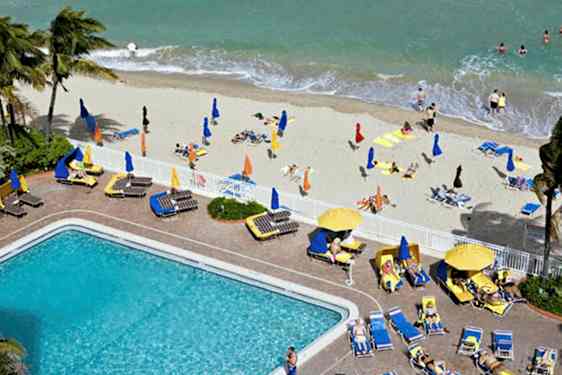 En strand med solsenger, parasoller og badende mennesker samt et basseng med omkringliggende solsenger. (AI-generert tekst)