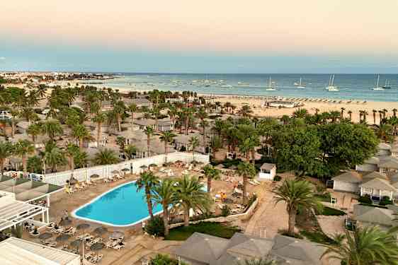 Luftfoto av hotellområde med basseng, palmer og en strand i bakgrunnen. (AI-generert tekst)