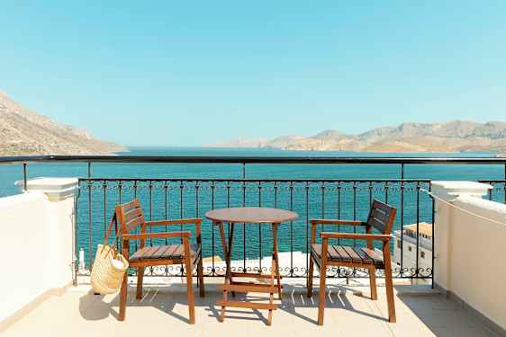 To trestoler og et bord på en terrasse med utsikt over havet og fjell i det fjerne. (AI-generert tekst)