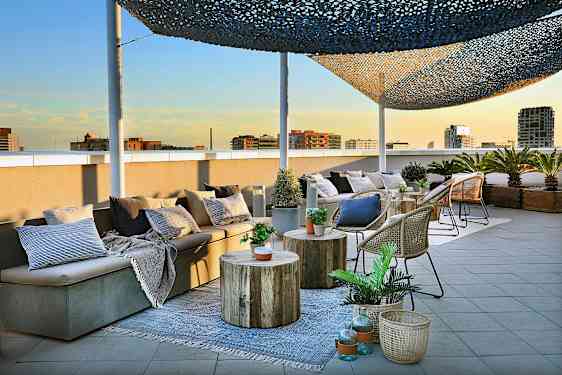 En takterrasse med sittemøbler, bord og kurver dekorert med planter og puter er avbildet. (AI-generert tekst)