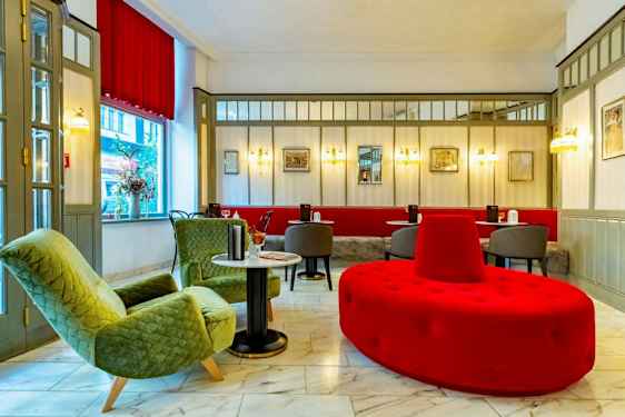 En hotellobby med sittegruppe inkludert grønne lenestoler, røde og grå sittemøbler og marmorgulv.  (AI-generert tekst)